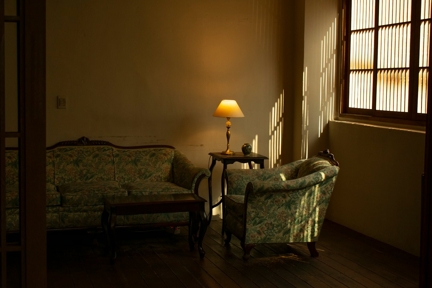 Ein floraler Sofas und Sessel stehen in einem sonnigen Wohnzimmer.